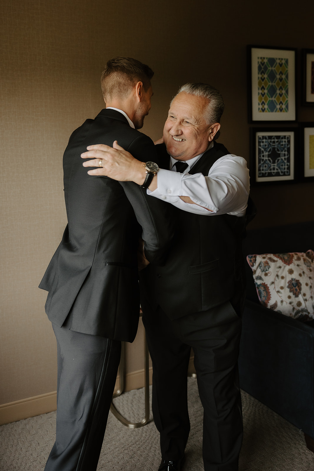 Groom hugs his father, who smiles warmly with pride during pre-wedding preparations.